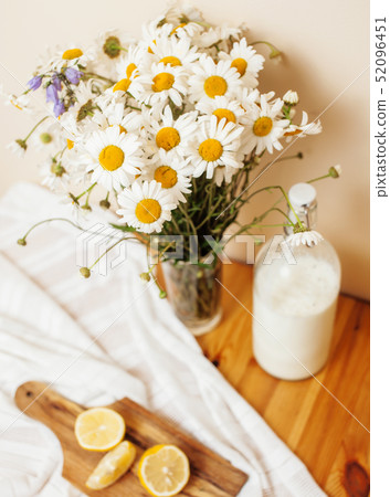 Simply stylish wooden kitchen with bottle of milk and glass on table, summer flowers camomile 52096451