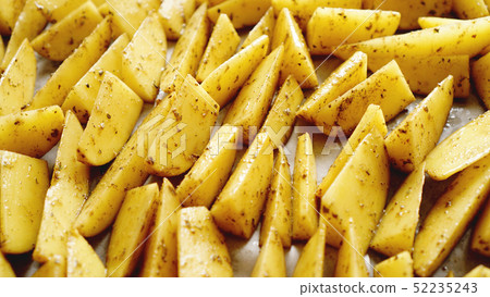 Sliced raw potatoes on a baking sheet with spices and rosemary, top view Sliced raw potatoes on a baking sheet with spices and rosemary, top view 52235243