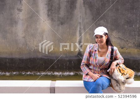 Portrait of young beautiful Asian woman sitting outdoors Portrait of young beautiful Asian woman sitting outdoors 52394596