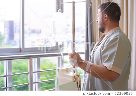 patient with a dropper looks out the window of the hospital room and smiles. back view. Healthcare patient with a dropper looks out the window of the hospital room and smiles. back view. Healthcare 52399055