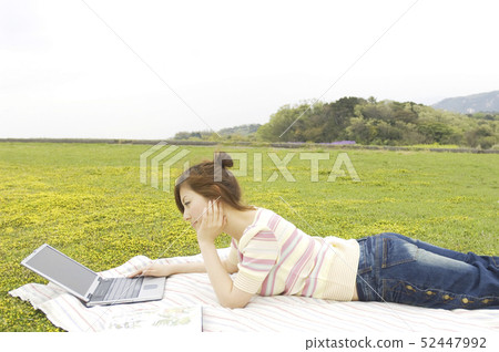 A woman who lays on a leisure sheet and uses a computer 52447992