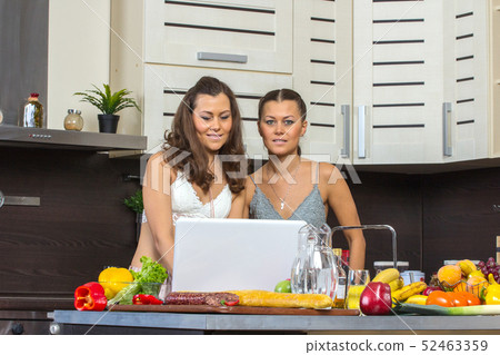 Two attractive twins women looking at laptop, standing in kitchen early morning. 52463359