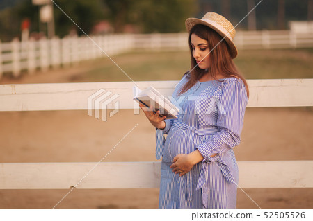 Beautiful pregnant woman read the book on the farm. She stand by the fance and look in to the book 52505526