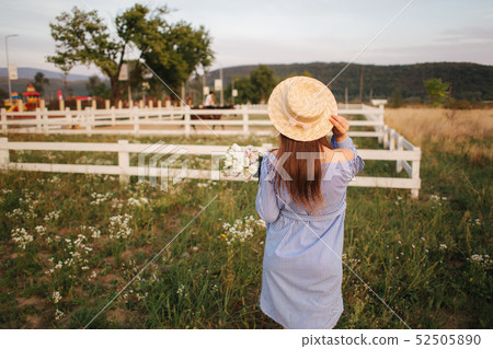 Back view of Beautiful lady. She hold a bouquet of flowers and smile. Background of farm 52505890