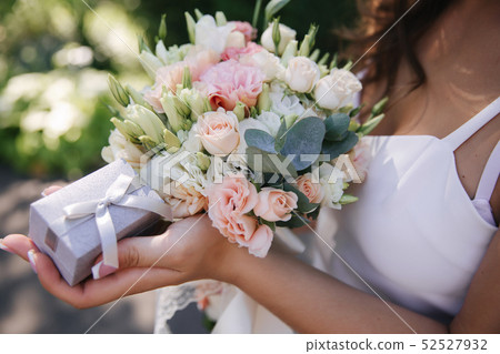 Girl hold a bouquet and ring box in hands. french manicure. Female is dressed in white dress Girl hold a bouquet and ring box in hands. french manicure. Female is dressed in white dress 52527932