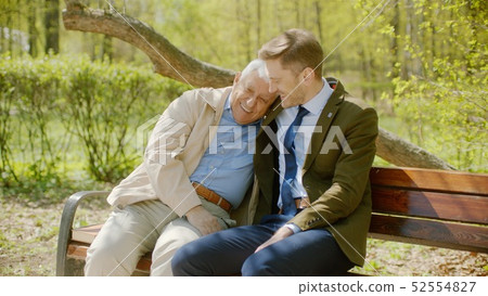 Youn man is hugging his old father on the bench in the autumn park Youn man is hugging his old father on the bench in the autumn park 52554827