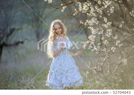 Cute blonde hair girl in a long winded dress, walking in blooming fruit garden. 52704043
