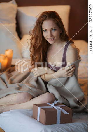 Girl lies on fluffy blanket and holds a Christmas gift above her 52727109