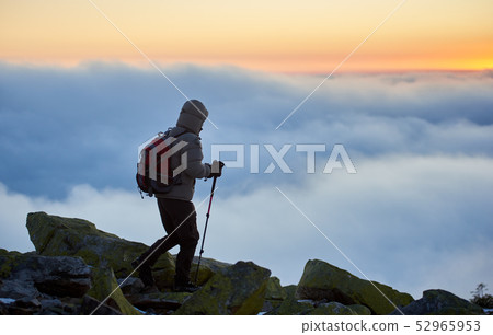 Tourist with backpack on rocky mountain on background of foggy valley and blue sky at sunrise. 52965953