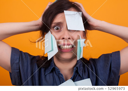 Portrait of beautiful woman frustrated with sticky notes on forehead in studio over yellow Portrait of beautiful woman frustrated with sticky notes on forehead in studio over yellow 52965973