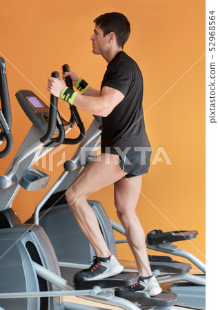 Side view of handsome man on elliptical trainer. 52968564
