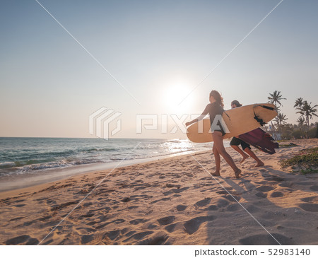 Young couple of happy smiling surfers run with surfboards on ocean coast, sport active lifestyle Young couple of happy smiling surfers run with surfboards on ocean coast, sport active lifestyle 52983140