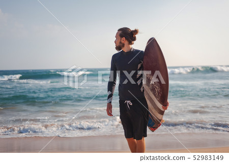 Young attractive sporty stylish man with a surfboard in hands against the background of the ocean Young attractive sporty stylish man with a surfboard in hands against the background of the ocean 52983149