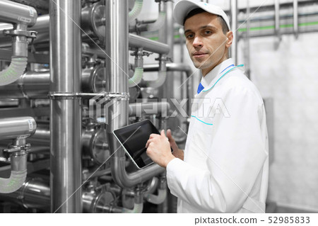 Portrait of man in a white robe and a cap standing in production department of dairy factory with Portrait of man in a white robe and a cap standing in production department of dairy factory with 52985833