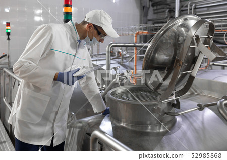 Inspector in a mask and a scrub stands with a folder-tablet in his hands at the dairy plant Inspector in a mask and a scrub stands with a folder-tablet in his hands at the dairy plant 52985868