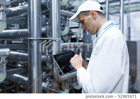 Portrait of man in a white robe and a cap standing in production department of dairy factory with Portrait of man in a white robe and a cap standing in production department of dairy factory with 52985871