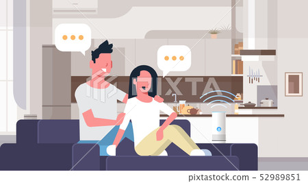 couple sitting on couch man woman using smartphone smart speaker voice recognition concept chat couple sitting on couch man woman using smartphone smart speaker voice recognition concept chat 52989851