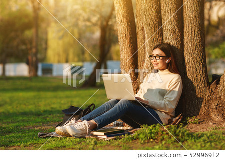 Student Girl Using Laptop Sitting Under Tree At University Campus 52996912