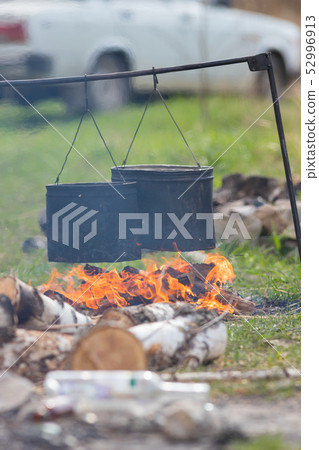 People heating up water in the metal buckets using a bonfire. Buckets hanging on the crossbar 52996913