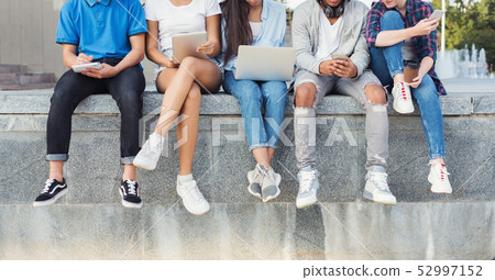 Company of teen friends sitting outdoor and using digital gadgets Company of teen friends sitting outdoor and using digital gadgets 52997152