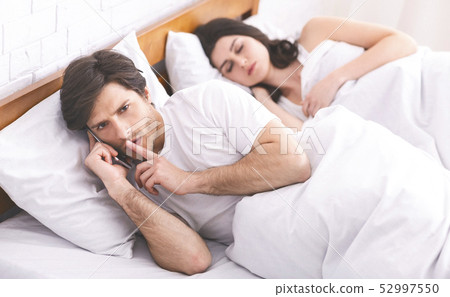Man cheater talking privately on cellphone in family bed Man cheater talking privately on cellphone in family bed 52997550