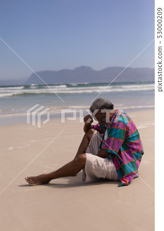 Senior man with hand on forehead sitting on beach 53000209