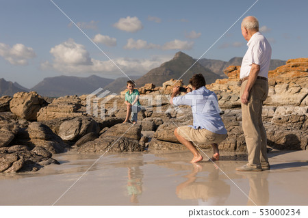 Father clicking photo of his son with mobile phone on beach Father clicking photo of his son with mobile phone on beach 53000234