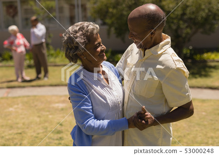 Side view of senior couple dancing together in garden 53000248