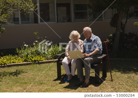 Front view of senior couple using laptop in garden Front view of senior couple using laptop in garden 53000284