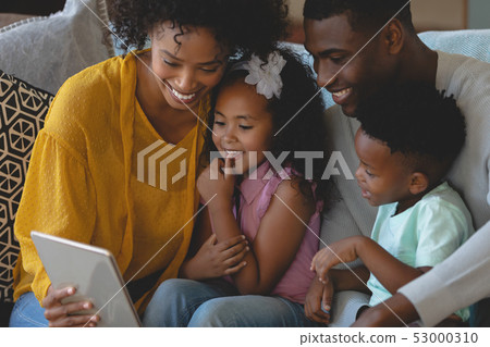 Happy African American parents with their cute children using digital tablet on sofa Happy African American parents with their cute children using digital tablet on sofa 53000310