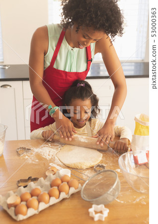 African American mother and daughter rolling out cookie dough in kitchen 53000363