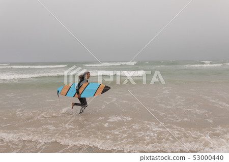 Senior female surfer with surfboard running on the beach 53000440