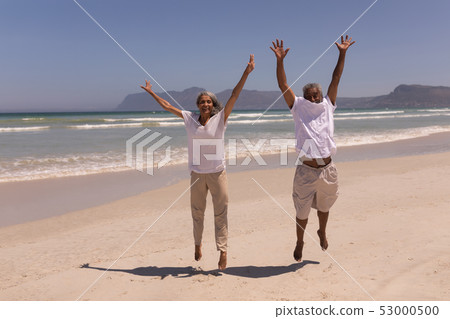 Senior couple with arms up jumping on beach  53000500
