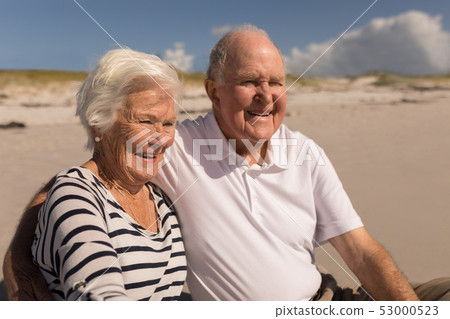 Happy senior couple sitting on beach Happy senior couple sitting on beach 53000523