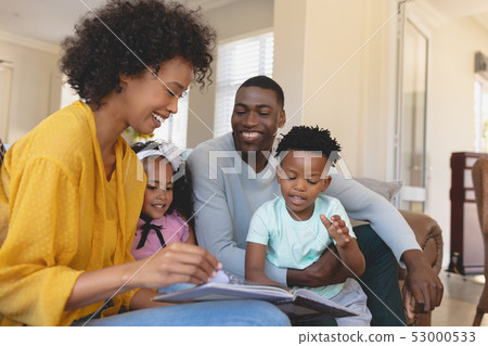 Happy African American parents with their cute children reading storybook on the sofa Happy African American parents with their cute children reading storybook on the sofa 53000533