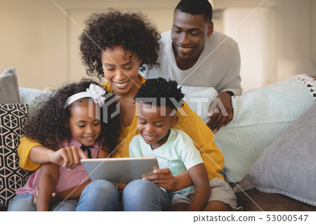 African American mother with her children using digital tablet on sofa while father looking them 53000547