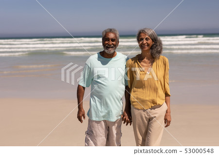 Senior couple holding hands and standing on beach 53000548