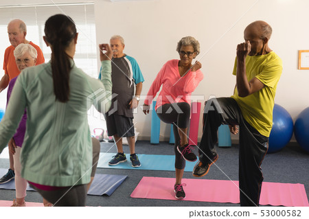 Rear view of female trainer assisting senior people in fitness studio Rear view of female trainer assisting senior people in fitness studio 53000582