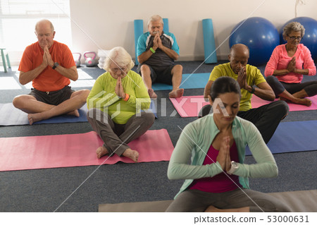 Senior people doing yoga with female trainer in fitness studio 53000631