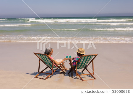 Senior couple relaxing on sun lounger and toasting cocktail glasses on beach Senior couple relaxing on sun lounger and toasting cocktail glasses on beach 53000658