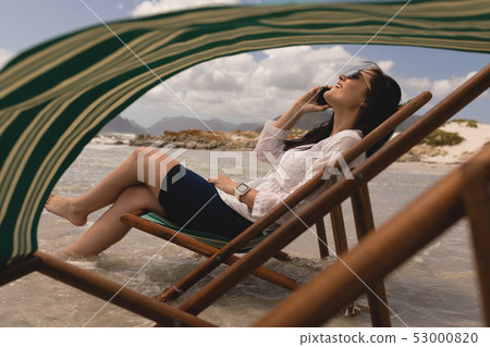 Young woman relaxing on sun lounger and talking on mobile phone Young woman relaxing on sun lounger and talking on mobile phone 53000820