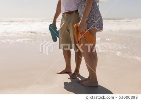 Young romantic couple holding beach footwear on beach Young romantic couple holding beach footwear on beach 53000899