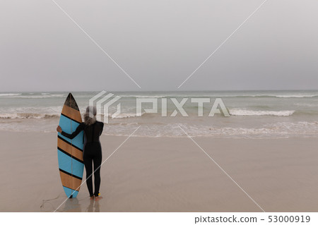 Senior female surfer with surfboard standing on the beach Senior female surfer with surfboard standing on the beach 53000919