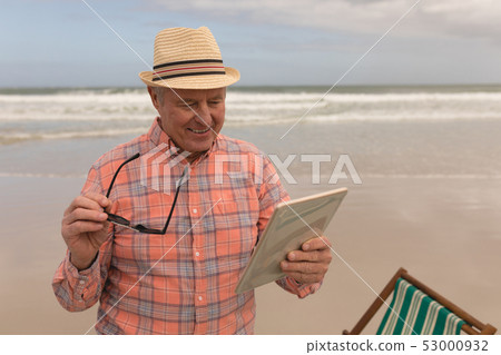Happy senior man using digital tablet at the beach Happy senior man using digital tablet at the beach 53000932
