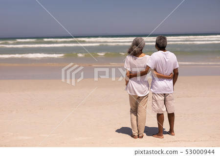 Senior couple standing on a beach with their arms around each other Senior couple standing on a beach with their arms around each other 53000944