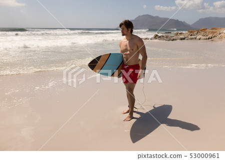 Shirtless young male surfer with surfboard standing on beach 53000961
