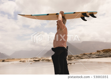 Senior man carrying surfboard on his head at beach 53001031