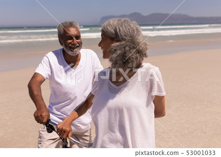 Senior couple standing with bicycle on beach Senior couple standing with bicycle on beach 53001033