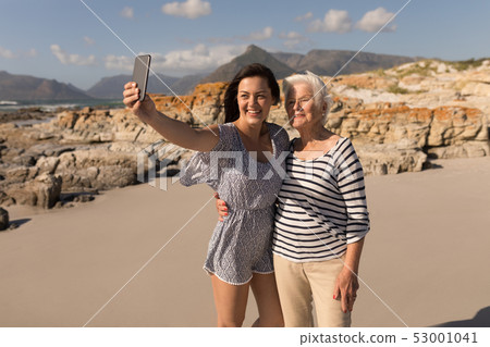 Happy young woman taking selfie with her mother on beach Happy young woman taking selfie with her mother on beach 53001041