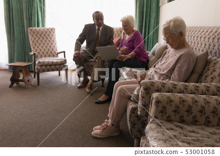 Side view of senior friends using digital tablet and laptop on sofa Side view of senior friends using digital tablet and laptop on sofa 53001058